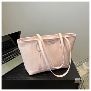 Dettaglio borsa tote rosa testurizzata con etichetta accanto a un laptop