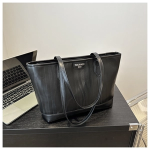 Dettaglio di una borsa tote nera con trama a onde e logo su una scrivania da ufficio
