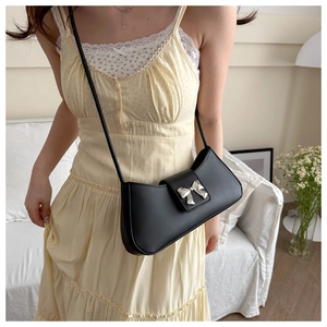 Detail of a black leather underarm bag with a silver metal bow buckle on a yellow dress