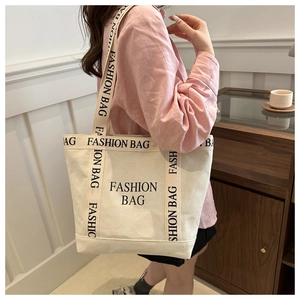 Detail shot of a beige canvas tote bag with 'FASHION BAG' print worn over the shoulder