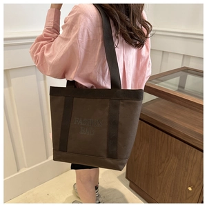Close-up of a large brown canvas tote bag with wide straps and Fashion Bag print