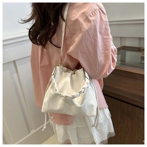 Detail view of white bucket bag featuring woven handle and drawstring details on a model