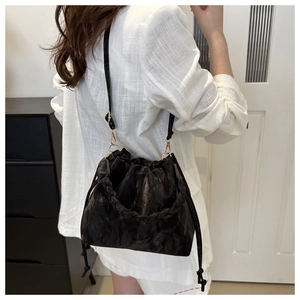 Detail of black drawstring bucket bag with woven handle and gold metal hardware hooks
