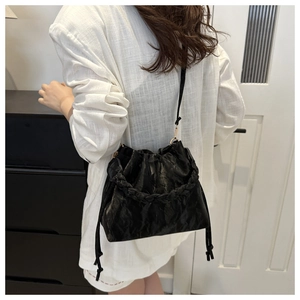 Detail of black pleated cloud bag with woven handle and adjustable strap on a white blazer