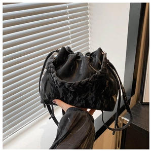 Detail of black pleated bucket bag featuring a braided handle and drawstring closure