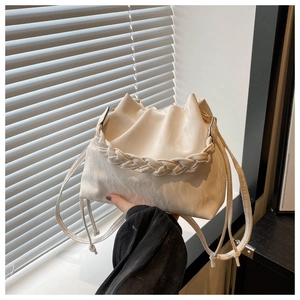 Detail of a creamy white bucket bag featuring woven handle and drawstring closure
