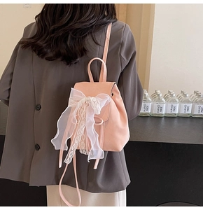 Détail d'un mini sac à dos rose clair avec un grand nœud en dentelle blanche et fines bretelles