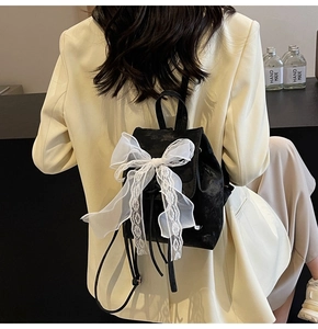 Détail d'un sac à dos noir avec un grand nœud en dentelle blanche et texture velours