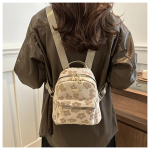 Detail of a beige mini backpack with brown floral print and golden zippers on a model