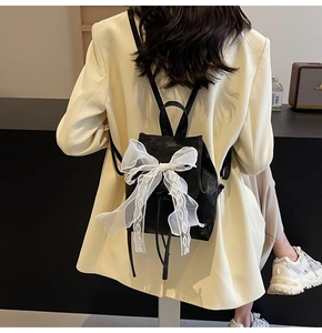 Détail d'un mini sac à dos noir avec un grand nœud en dentelle blanche et cordon de serrage