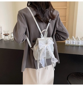 Mini sac à dos argenté avec un grand nœud en dentelle blanche porté par un mannequin