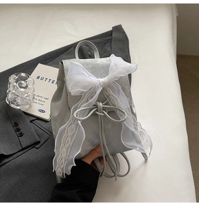 Détail du mini sac à dos argenté avec un grand nœud en dentelle blanche et cordon