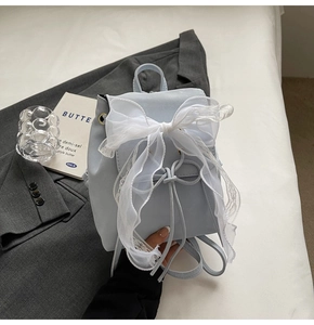 Détail d'un mini sac à dos bleu clair avec un grand nœud en dentelle blanche et cordon de serrage