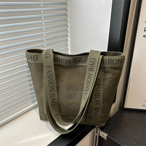 Olive green canvas tote bag with fashion lettering displayed on a minimalist window sill