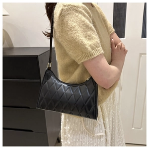 Détail d'un sac porté épaule noir matelassé avec finitions dorées et coutures en losange