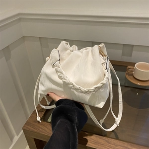 Elegant white drawstring bucket bag with pleated texture and woven handle in lifestyle setting