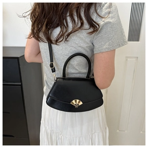 Détail d'un sac bandoulière en cuir noir avec un fermoir doré en forme d'éventail