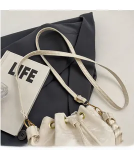 Detail of cream drawstring bucket bag showing smooth shoulder strap and metal eyelets