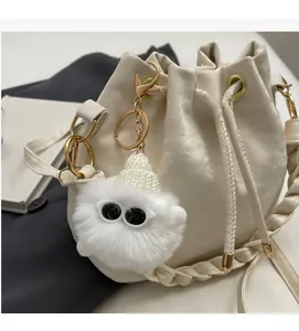 Detail of cream woven bucket bag with drawstring closure and cute plush monster charm