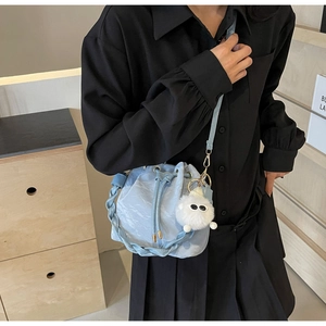 Detail of light blue drawstring bucket bag with woven handle and plush charm on model