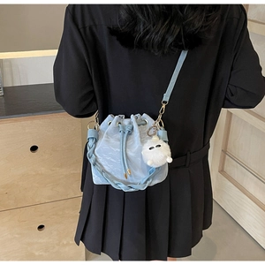 Close-up of light blue drawstring bucket bag with fuzzy white charm and braided handle