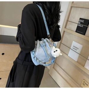 Detail of light blue drawstring bucket bag with pleated texture and white plush charm
