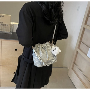 Detail of silver metallic drawstring bucket bag with fuzzy monster charm and woven handle