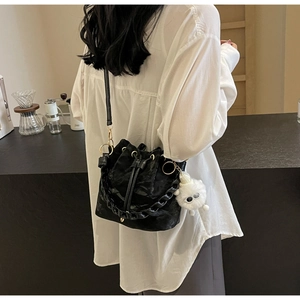 Detail of black drawstring bucket bag with pleated texture and fuzzy monster charm