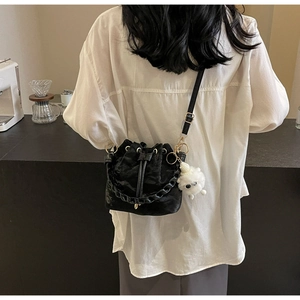 Detail of a black drawstring bucket bag with a chain strap and plush monster charm