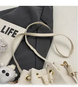 Detail of cream drawstring bucket bag showing adjustable shoulder strap and gold hardware