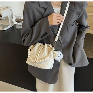 Detail of cream drawstring bucket bag with braided handle and plush charm on a gray blazer