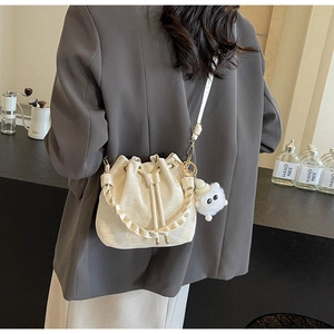 Detail of cream drawstring bucket bag with braided handle and plush charm on a model