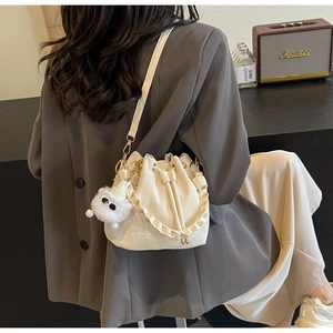 Detail view of white drawstring bucket bag with leather texture and plush charm