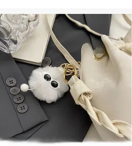 Detail of cream drawstring bucket bag featuring a fuzzy plush monster charm with sunglasses