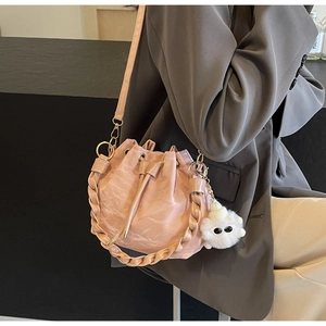 Detail of pink drawstring bucket bag with woven handle and plush charm on a model