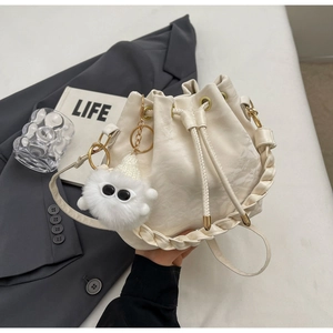 Close-up of off-white leather bucket bag with woven handle and plush charm detail