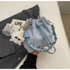 Detail of light blue bucket bag with woven handle, marble texture and plush monster charm