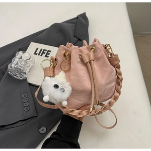 Pink drawstring bucket bag with pleated texture, woven handle and plush monster charm