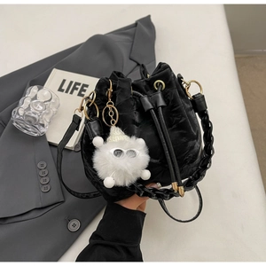 Detail of black velvet bucket bag with woven handle and quirky plush doll charm