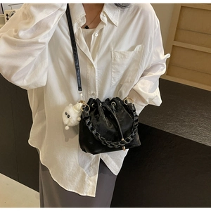 Detail of black drawstring bucket bag featuring a woven strap and plush white pompom charm