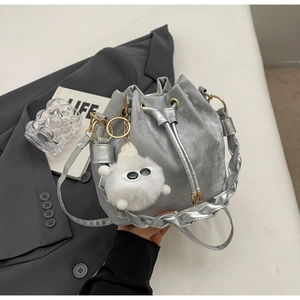 Detailed view of silver drawstring bucket bag with plush monster charm and woven handle