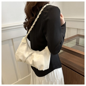Detail view of cream pleated shoulder bag featuring a woven strap and half-moon silhouette