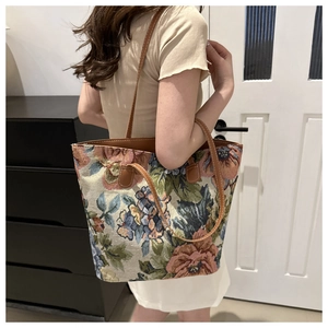 Detail of floral tapestry tote bag with brown leather handles worn by a model