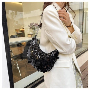 Detail view of a black sequin hobo bag with a thin metal chain strap on a white blazer