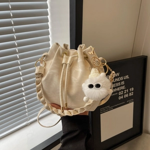 Chic beige drawstring bucket bag with soft leather texture and plush glasses charm