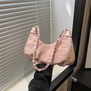 Pink pleated crescent shoulder bag with woven handle shown under natural light and shadows
