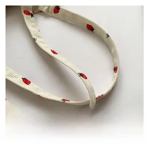 Detail of cream corduroy shoulder strap featuring red strawberry prints and gold metal rings