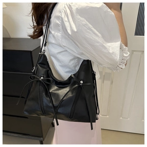 Detail of black PU leather shoulder bag featuring ribbon bows and silver zippers on a model