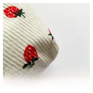 Close-up of corduroy fabric texture with detailed red strawberry embroidery pattern