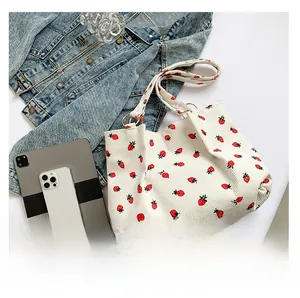 Detail of white corduroy tote bag with strawberry print and wide strap on desk